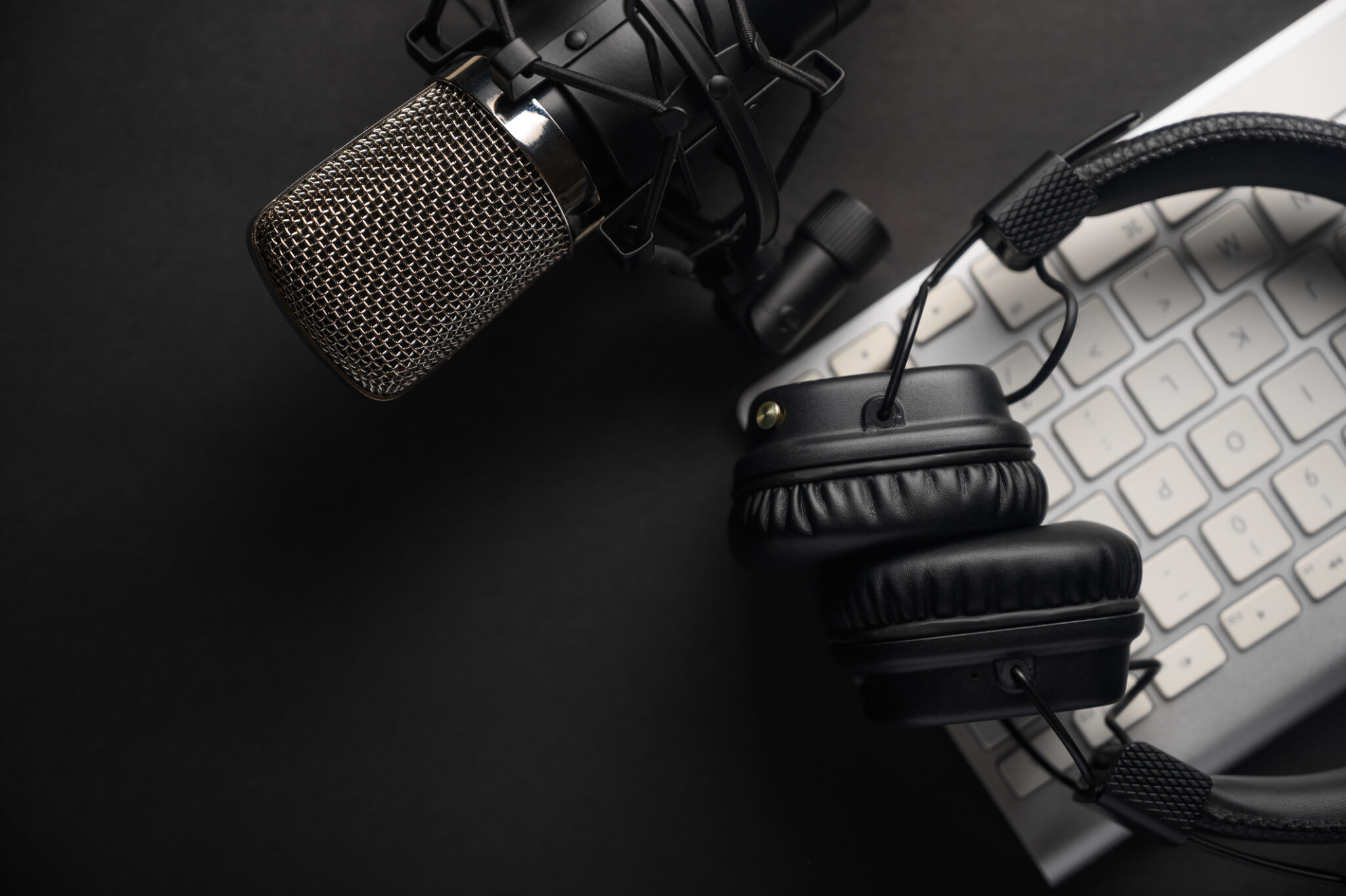 Flat lay, Studio microphone with professional headphones on a PC keyboard. Black on a black background. Podcasts, radio, streams, blogging, working with sound, recording tracks